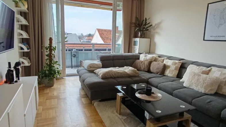 Helles Wohnzimmer mit großem Ecksofa, Parkettboden und Zugang zum Balkon.