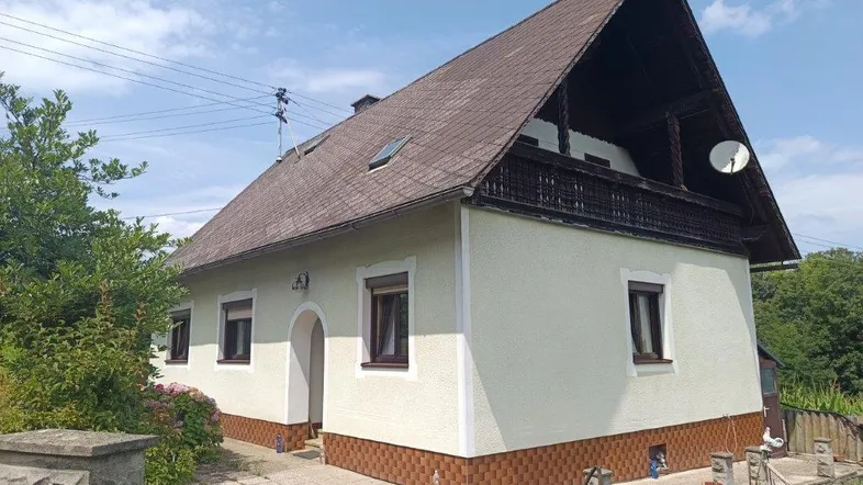 Traditionelles Einfamilienhaus mit Satteldach, Balkon und heller Fassade in ländlicher Umgebung.