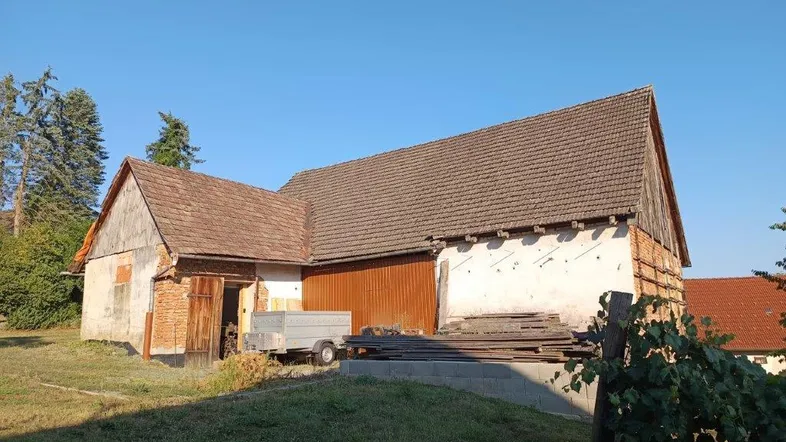 Altes Scheunengebäude mit Holztüren und Ziegeldach, umgeben von Grünflächen unter blauem Himmel.