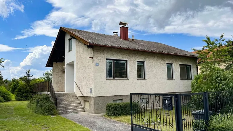 Einfamilienhaus mit heller Fassade, Satteldach und Außentreppe unter bewölktem Himmel.