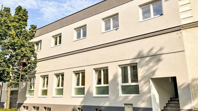 Moderne Fassade eines Mehrfamilienhauses mit hellen Putzflächen und dunklem Dach.