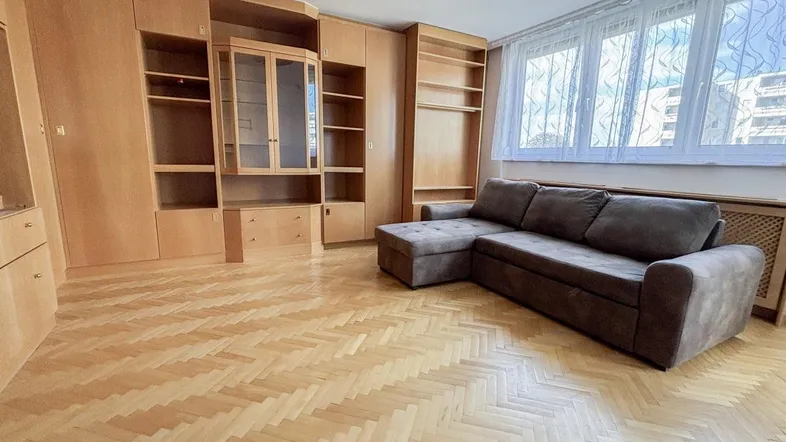 Helles Wohnzimmer mit Fischgrätparkett, großem Wandschrank und bequemer Couch.