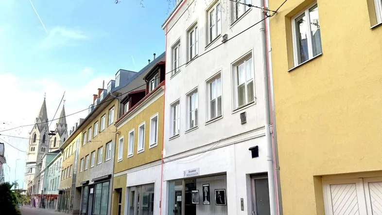 Eine Reihe von Gebäuden entlang einer gepflasterten Straße mit einem Kirchturm im Hintergrund unter blauem Himmel.