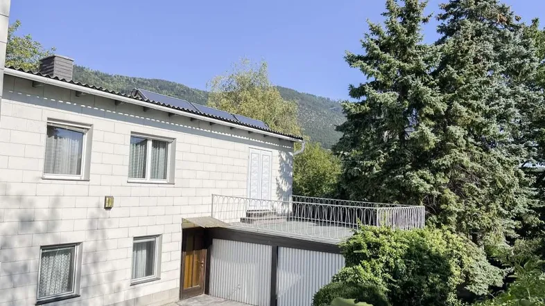 Ansicht des Hauses mit Garage, einer Terrasse im Obergeschoss und umgebender Natur.