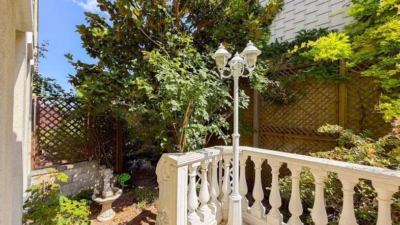 Kleiner, gepflegter Gartenbereich mit klassischer Balustrade und Laterne, umgeben von üppigem Grün.