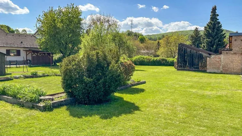 Großer, gepflegter Garten mit weitläufiger Rasenfläche, Bäumen und Sträuchern unter blauem Himmel.