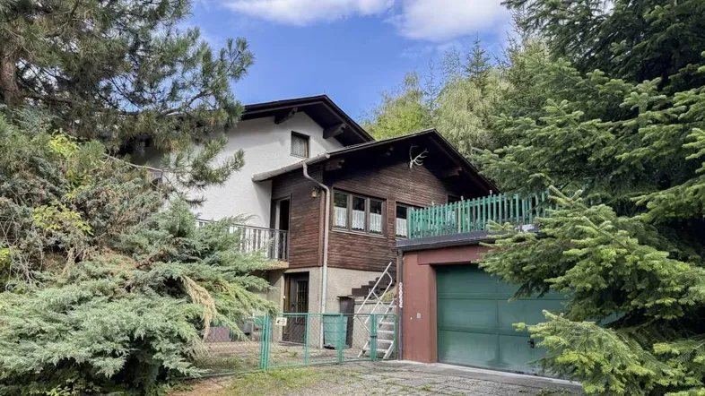Traditionelles Haus mit Holzfassade und integrierter Garage, umgeben von viel Grün.