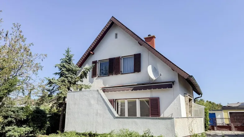 Einfamilienhaus mit Satteldach, Fensterläden und Satellitenschüssel in ländlicher Umgebung.