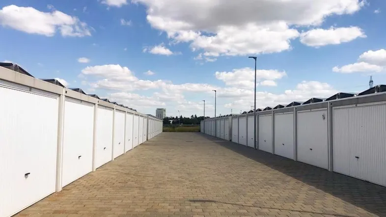 Lange Reihen von weißen Garagen mit gepflastertem Zufahrtsweg unter blauem Himmel mit Wolken.