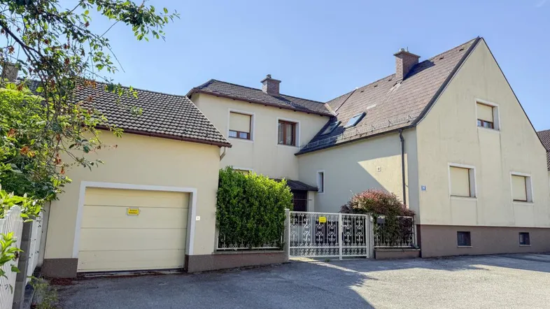 Vorderansicht des Hauses mit Garage, Einfahrt und schmiedeeisernem Tor.