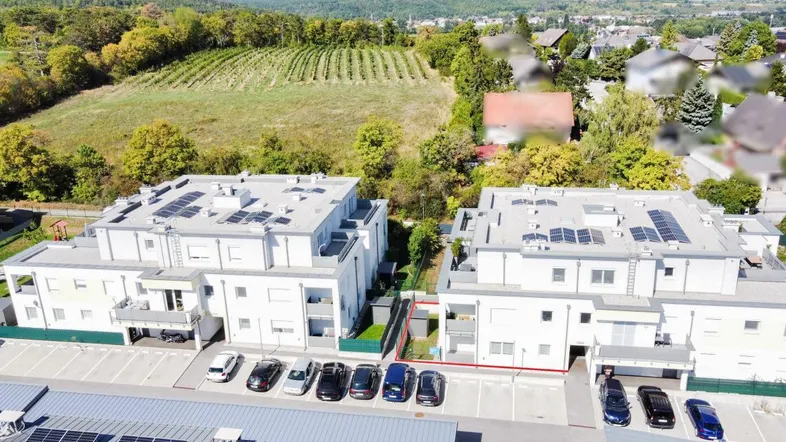 Luftaufnahme von modernen Wohngebäuden mit Solaranlagen, Parkplätzen und Weinbergen im Hintergrund.