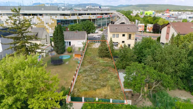Luftaufnahme eines unbebauten Grundstücks mit roter Umrandung, umgeben von Häusern und einem Einkaufszentrum.