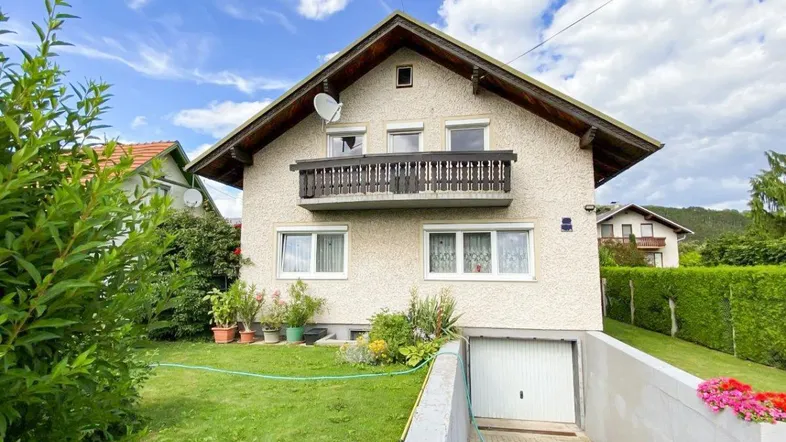 Einfamilienhaus mit gepflegtem Garten, Balkon und integrierter Garage unter blauem Himmel.