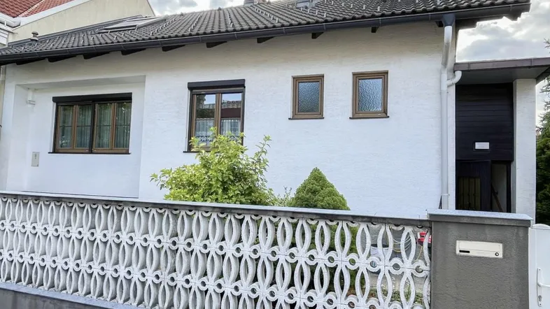 Vorderansicht des Hauses mit weißer Fassade, braunen Fenstern und einem dekorativen Zaun.
