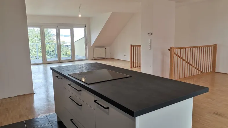 Offener Wohnbereich mit moderner Kücheninsel, Parkettboden und Zugang zu einem sonnigen Balkon.