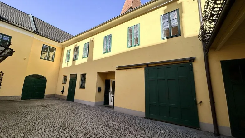Ein sonniger Innenhof mit Kopfsteinpflaster und gelben Fassaden, umgeben von historischen Gebäuden mit grünen Türen und Fenstern.