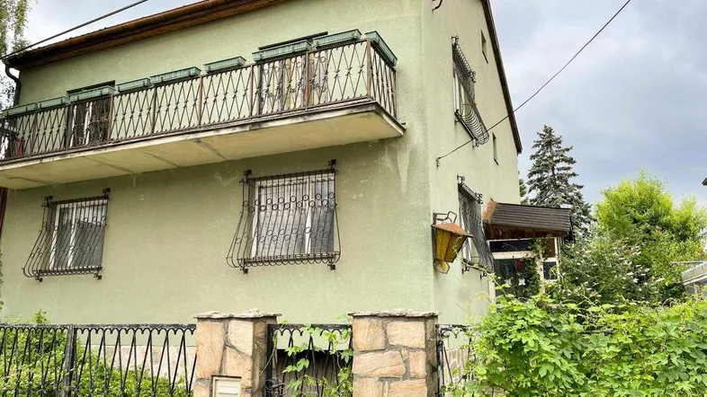 Altes Wohnhaus mit grüner Fassade, Balkon und schmiedeeisernen Fenstergittern.