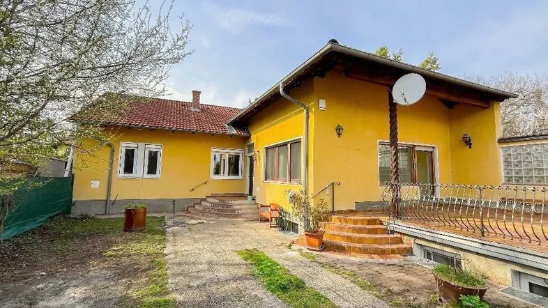 Gelbes Einfamilienhaus mit rotem Ziegeldach, Vorgarten und gepflasterter Auffahrt.