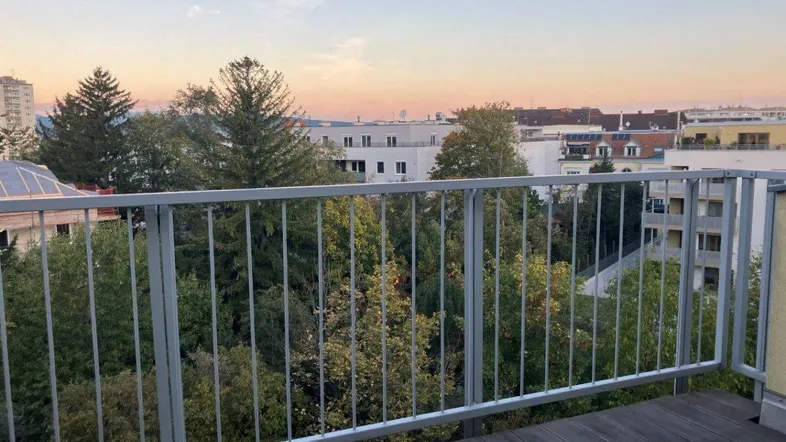 Balkon mit Holzdielen und Metallgeländer bei Sonnenuntergang, bietet einen weiten Blick über die Stadt.