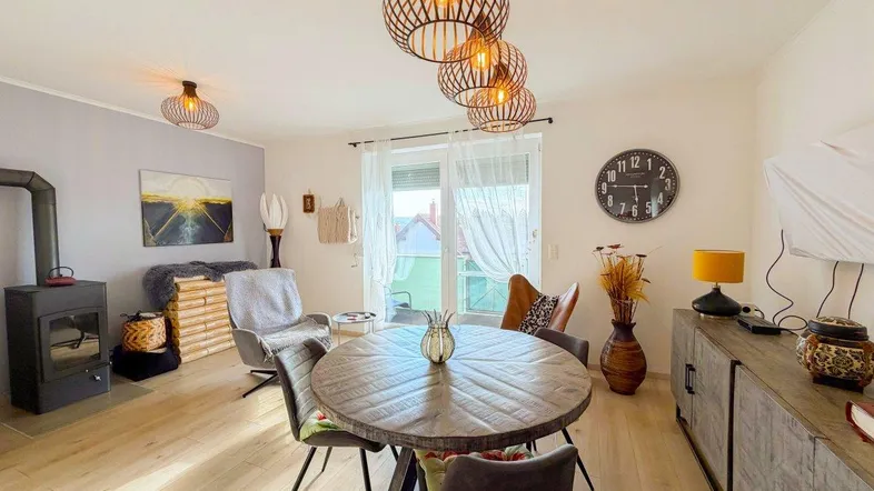Heller Wohn- und Essbereich mit Holzboden, Kaminofen und Zugang zum Balkon.
