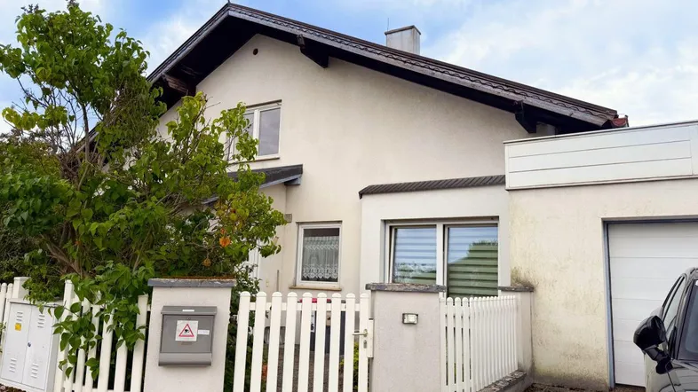 Vorderansicht eines Einfamilienhauses mit weißem Zaun und Vorgartenbereich.
