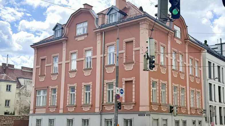 Historisches Gebäude an einer Straßenecke mit markanter Fassade und angrenzendem Neubau.