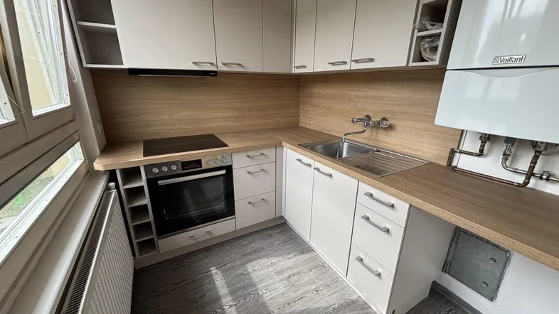 Moderne Küche mit hellen Schränken, Holzarbeitsplatten, integriertem Backofen und Induktionskochfeld.