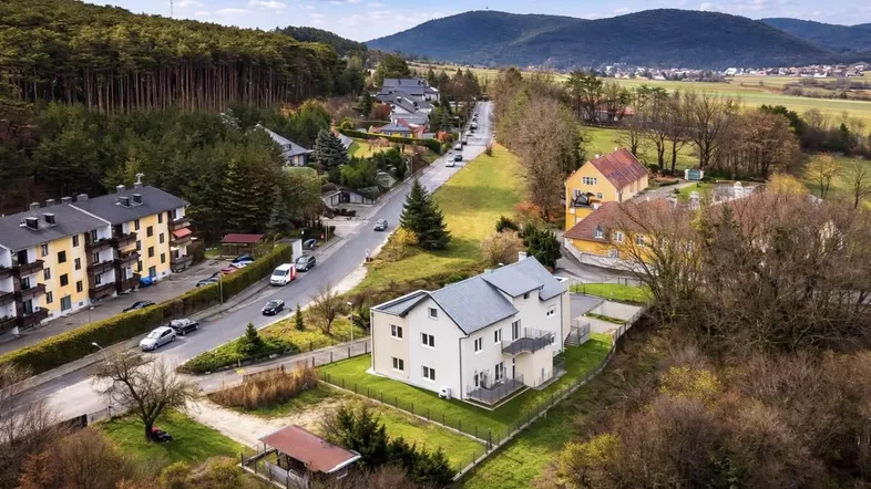 Luftaufnahme eines modernen Wohnhauses in ländlicher Umgebung mit Wald und Bergen im Hintergrund.