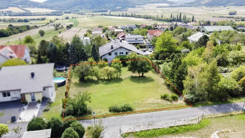 Luftaufnahme eines Baugrundstücks mit roter Umrandung, umgeben von Häusern und grüner Landschaft.