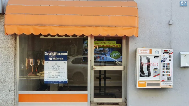 Vorderansicht eines Geschäftsraums mit orangefarbener Markise und Schaufenster zur Straße.