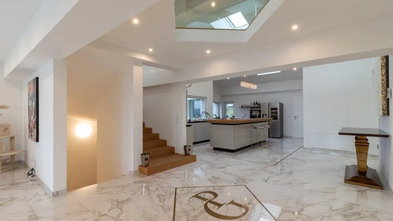 Großzügiger Eingangsbereich mit Marmorboden, offener Treppe und Blick in die moderne Küche.