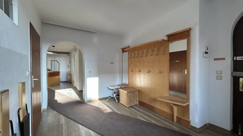 Geräumiger Flur mit Garderobe, Holzvertäfelung und Laminatboden, der zu weiteren Räumen führt.