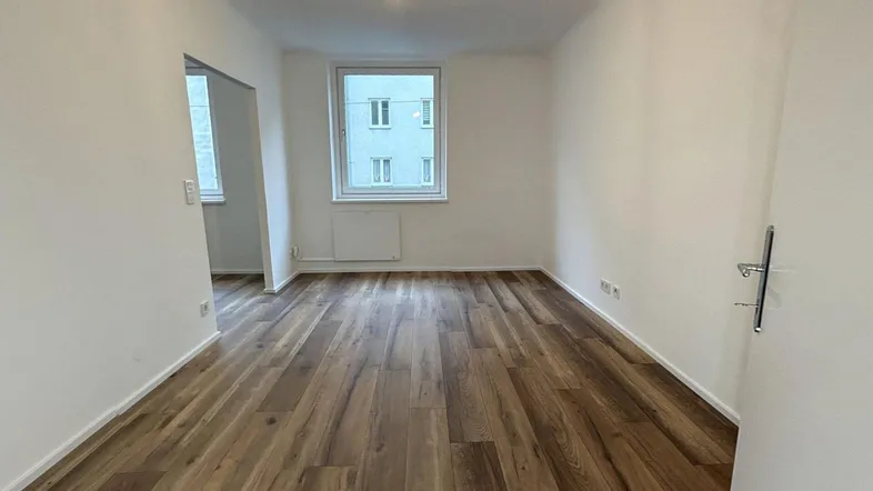 Helles, leeres Zimmer mit neuem Laminatboden und weißen Wänden, bereit zur individuellen Gestaltung.