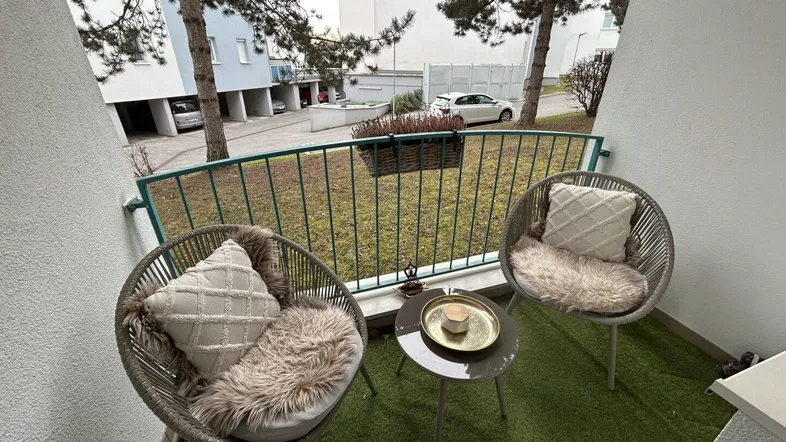 Gemütlicher Balkon mit Kunstrasen, bequemen Sitzgelegenheiten und Blick ins Grüne.