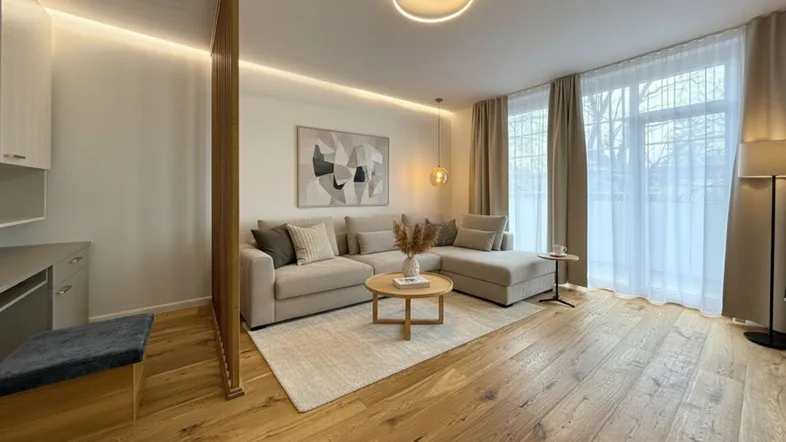 Modernes Wohnzimmer mit beigem Ecksofa, Holzboden und großen Fenstern, die viel Licht hereinlassen.