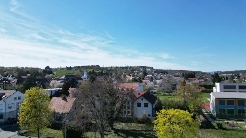 Panoramablick über eine Wohngegend mit Häusern, Bäumen und einer Straße unter blauem Himmel.