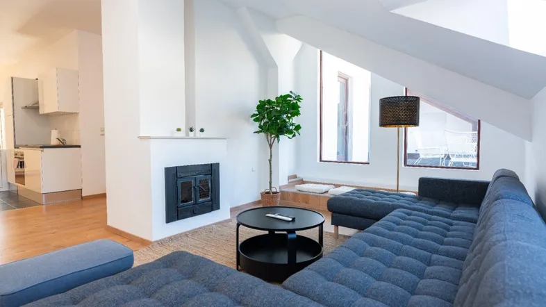 Helles Wohnzimmer mit gemütlichem Sofa, Kamin und Dachschrägenfenster, offen zur Küche.
