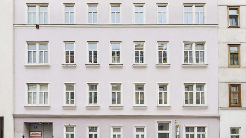Fassade eines Mehrfamilienhauses mit mehreren Fenstern und parkenden Autos davor.