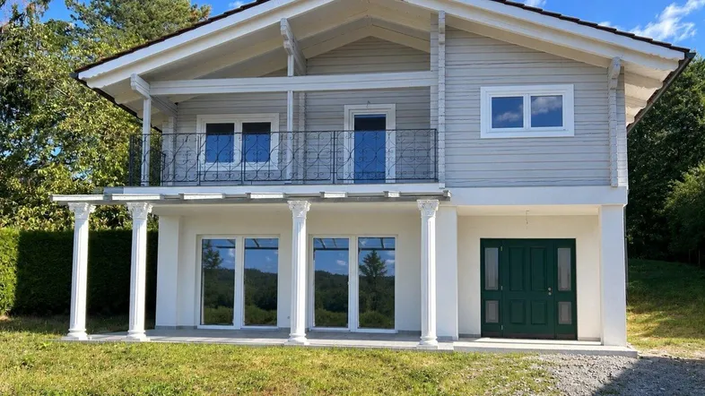 Modernes Einfamilienhaus mit heller Holzfassade, Balkon und überdachter Terrasse.