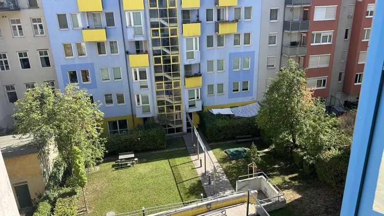 Blick von oben auf den begrünten Innenhof mit Rasenfläche, Bäumen und einem Spielbereich.
