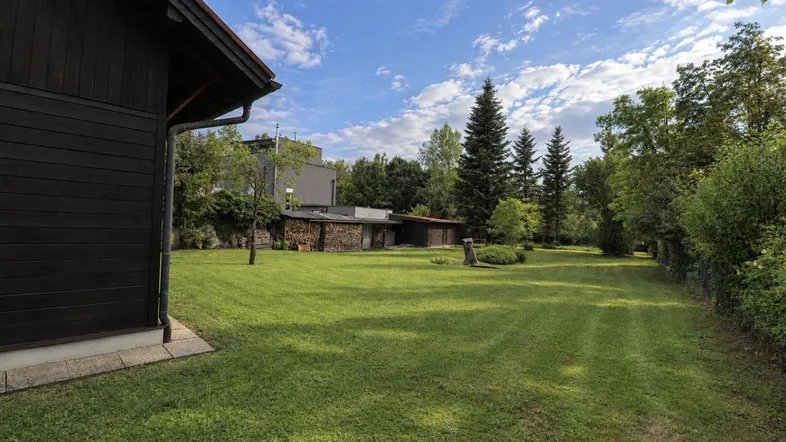 Großer, gepflegter Garten mit Rasenfläche, Holzschuppen und Baumbestand unter blauem Himmel.