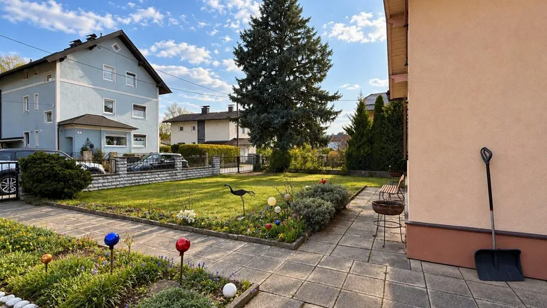 Gepflegter Vorgarten mit Rasenfläche, Blumenbeeten und einem großen Nadelbaum vor einem Wohnhaus.