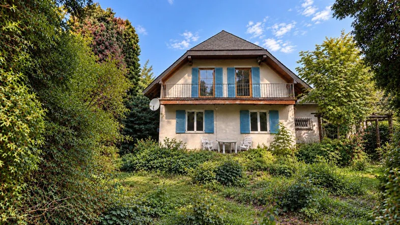 Einfamilienhaus mit Satteldach und Balkon, umgeben von einem üppigen, grünen Garten.