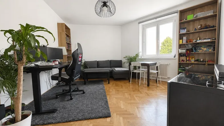 Helles Wohnzimmer mit Parkettboden, Schreibtischbereich, gemütlichem Sofa und großem Fenster.