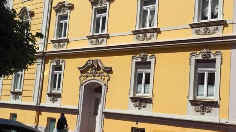 Historisches Gebäude mit gelber Fassade, verzierten Fenstern und Eingangsbereich.