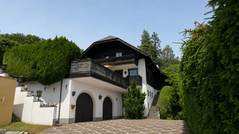 Traditionelles Haus mit Balkon, Doppelgarage und gepflasterter Auffahrt, umgeben von viel Grün.