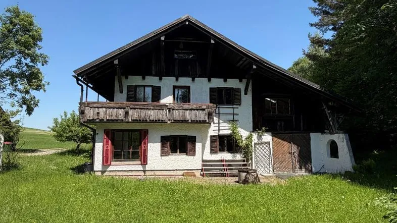 Traditionelles bayerisches Bauernhaus mit Holzbalkon und weißer Fassade, umgeben von grünen Wiesen.