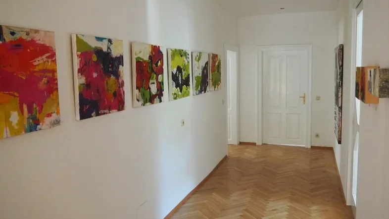 Heller Flur mit weiß gestrichenen Wänden, Fischgrätparkett und farbenfrohen Kunstwerken an der Wand.
