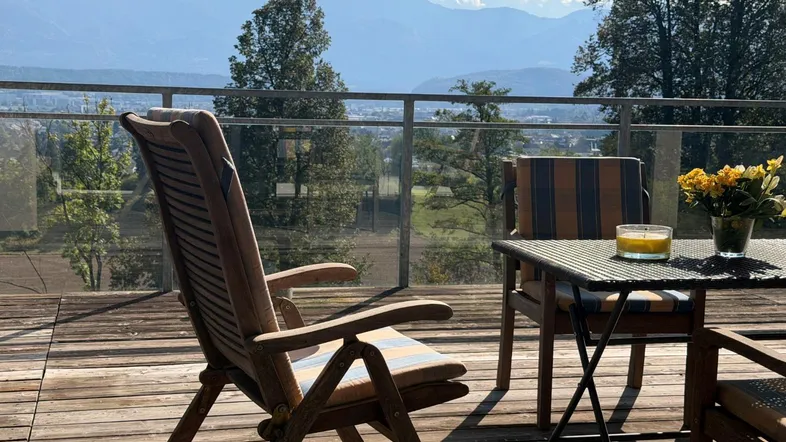 Große Holzterrasse mit Gartenmöbeln und einem weiten Blick auf die Berge und das Tal.