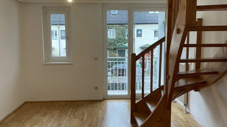 Helles Zimmer mit Holztreppe, Parkettboden und Zugang zu einem kleinen Balkon.